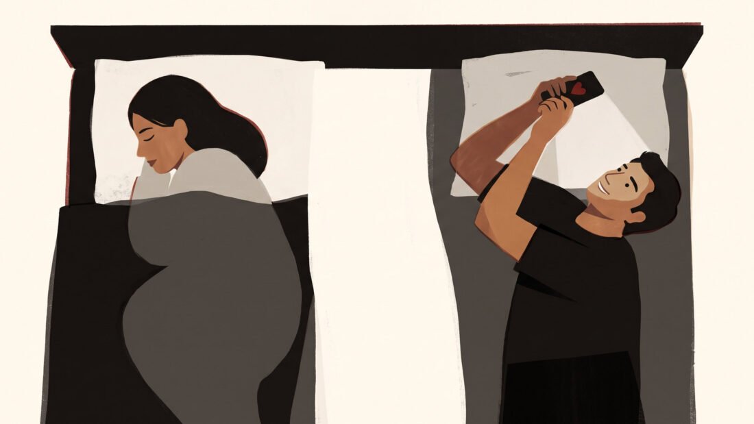 A couple in bed seen from above. She sleeps facing away. He lies awake, smiling up at the phone held over his face.